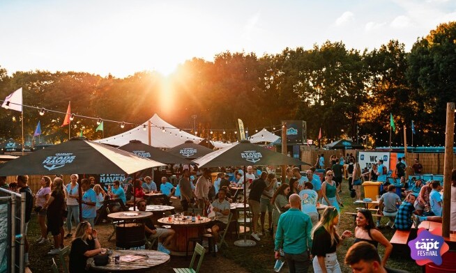 Mensen genieten van een muziekfestival in het park met foodtrucks en zonsondergang.