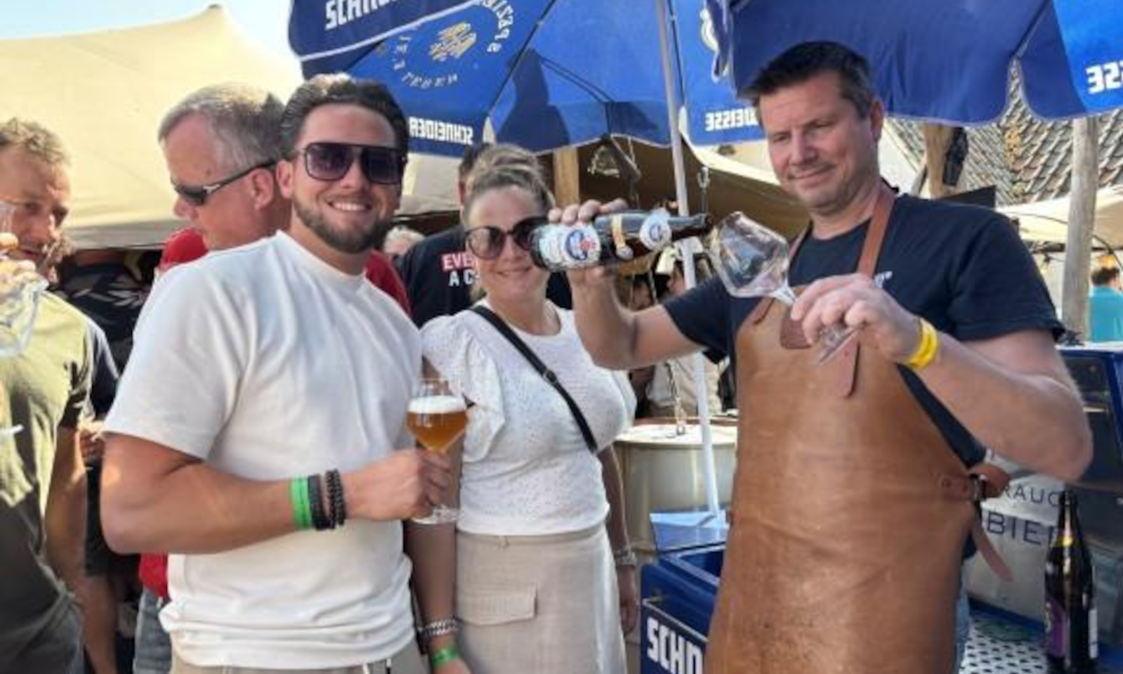 Mensen genieten van bier bij een stand met blauwe parasols op een bierfestival.