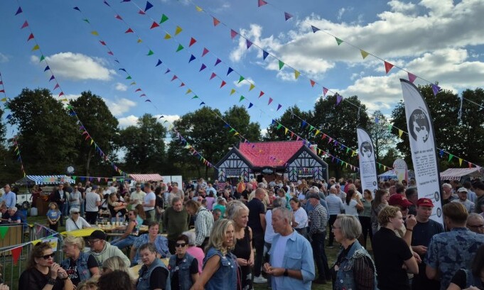 Drukke openlucht festival met feestelijke vlaggetjes en een grote menigte voor een huis in Tudorstijl.
