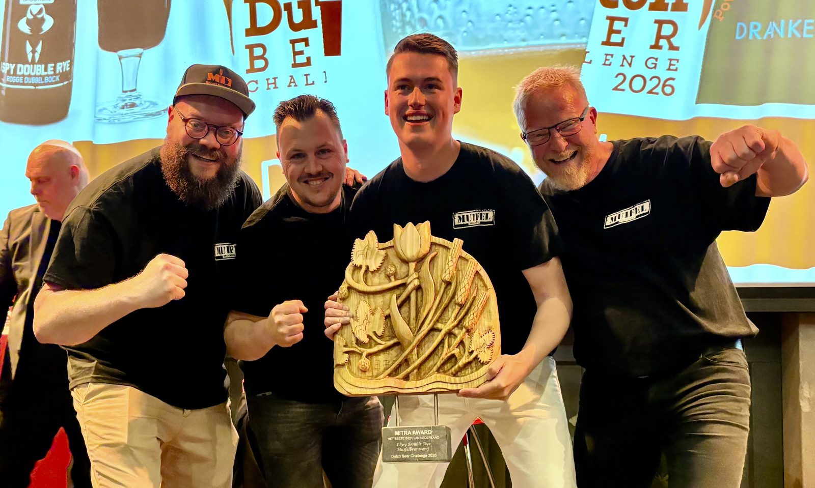 Vier mannen die een houten trofee vasthouden op een podium tijdens een prijsuitreiking.