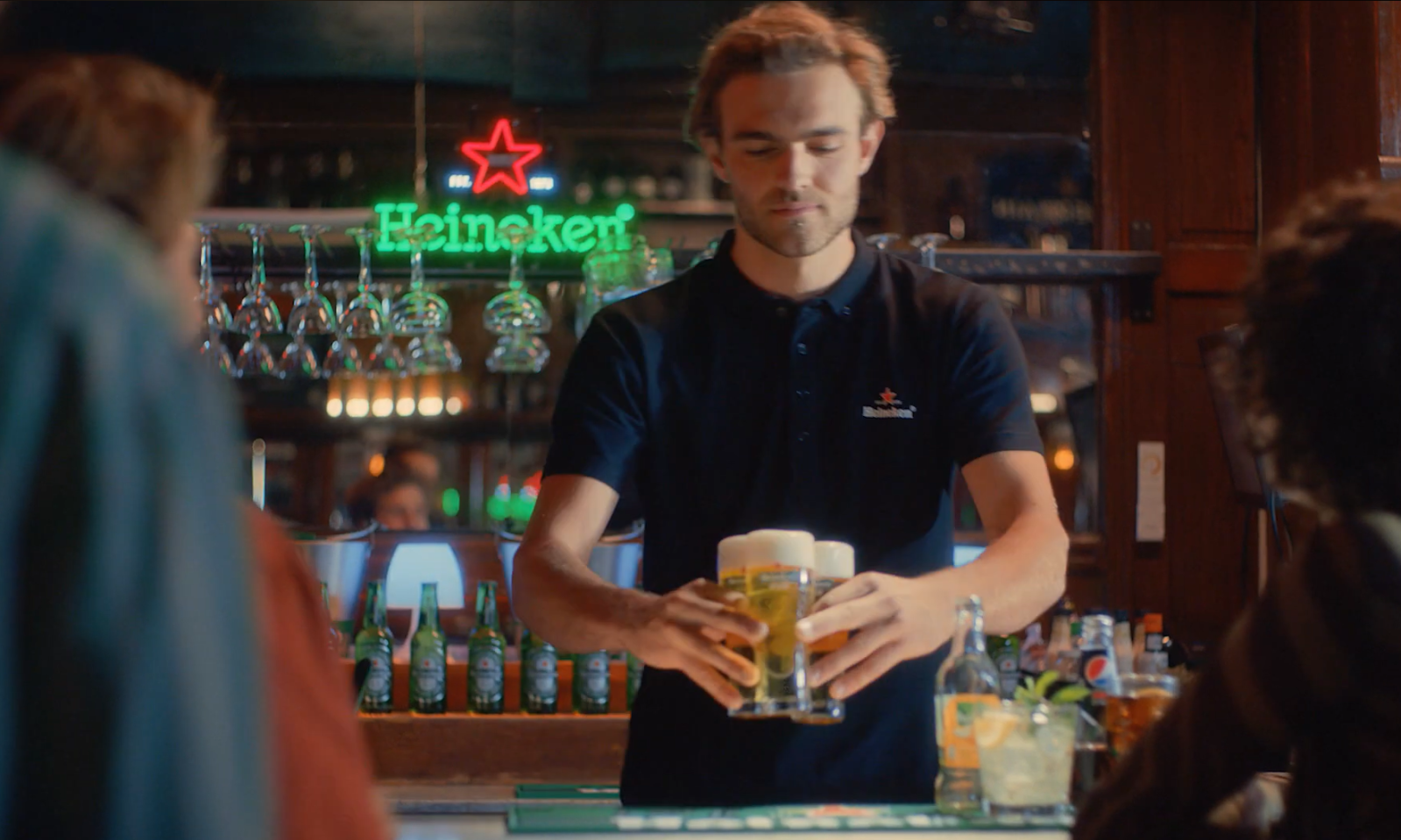 Barman in bar schenkt twee glazen bier in bij een toog met Heineken bord.