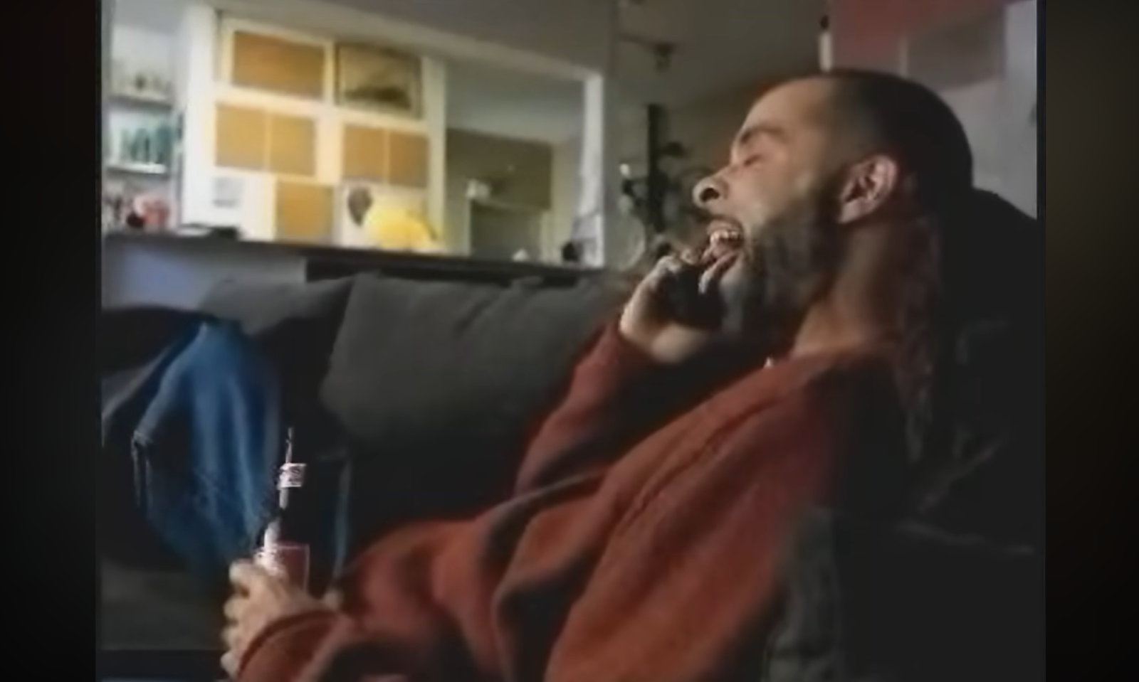 Man lacht op bank terwijl hij met telefoon en bier praat