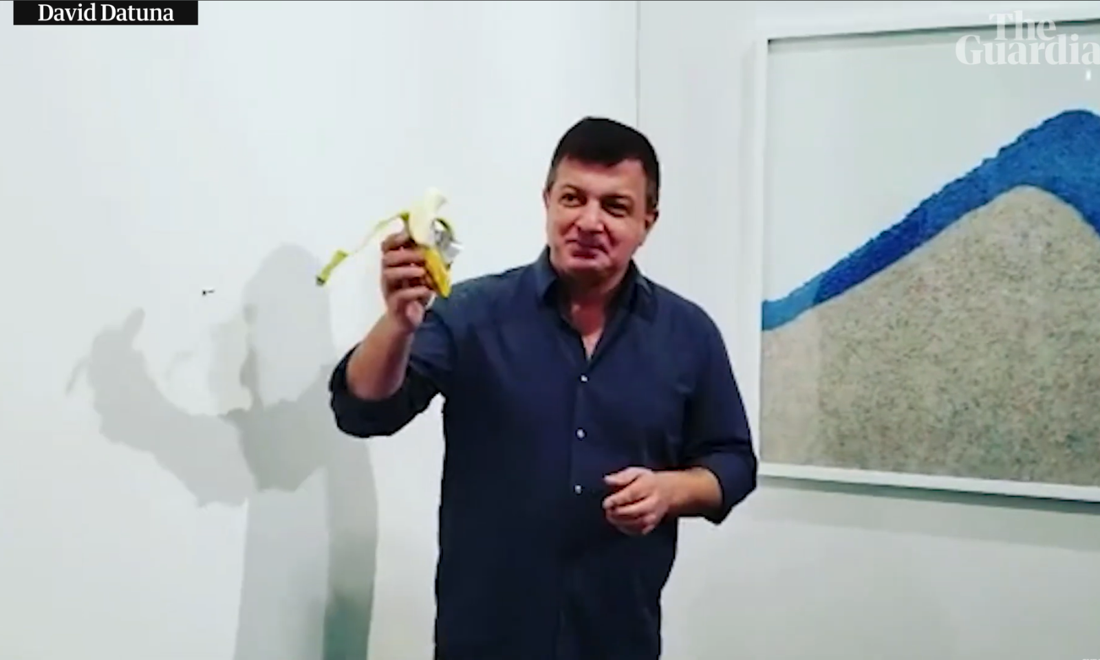 Man met een geschilde banaan voor een kunstwerk in een gallery.