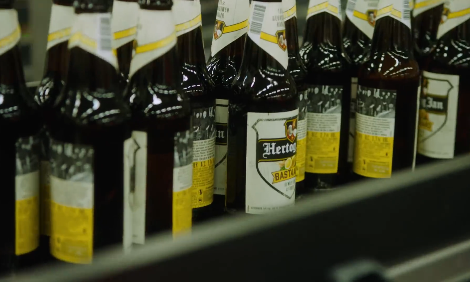 Rij flessen Hertog Jan Bastaard bier op een lopende band in een brouwerij.
