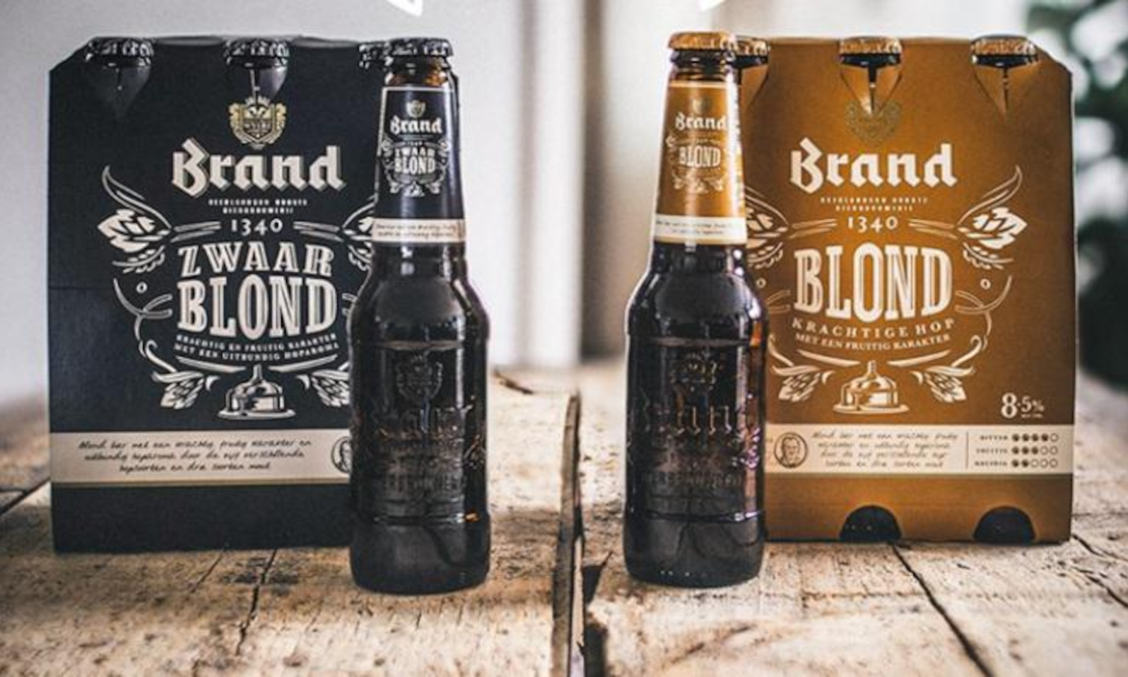 Twee flessen bier voor Brand Zwaar Blond en Brand Blond verpakking op houten tafel.