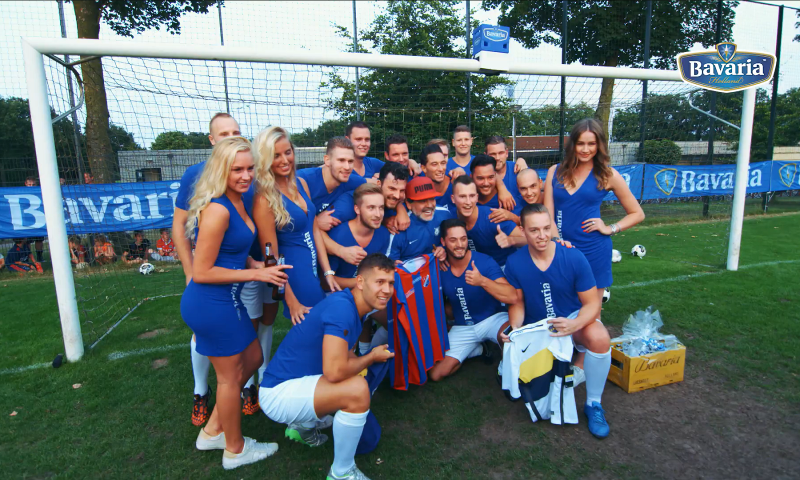 Groep mensen in blauwe sportkleding poseert voor een doel met Bavaria banners.
