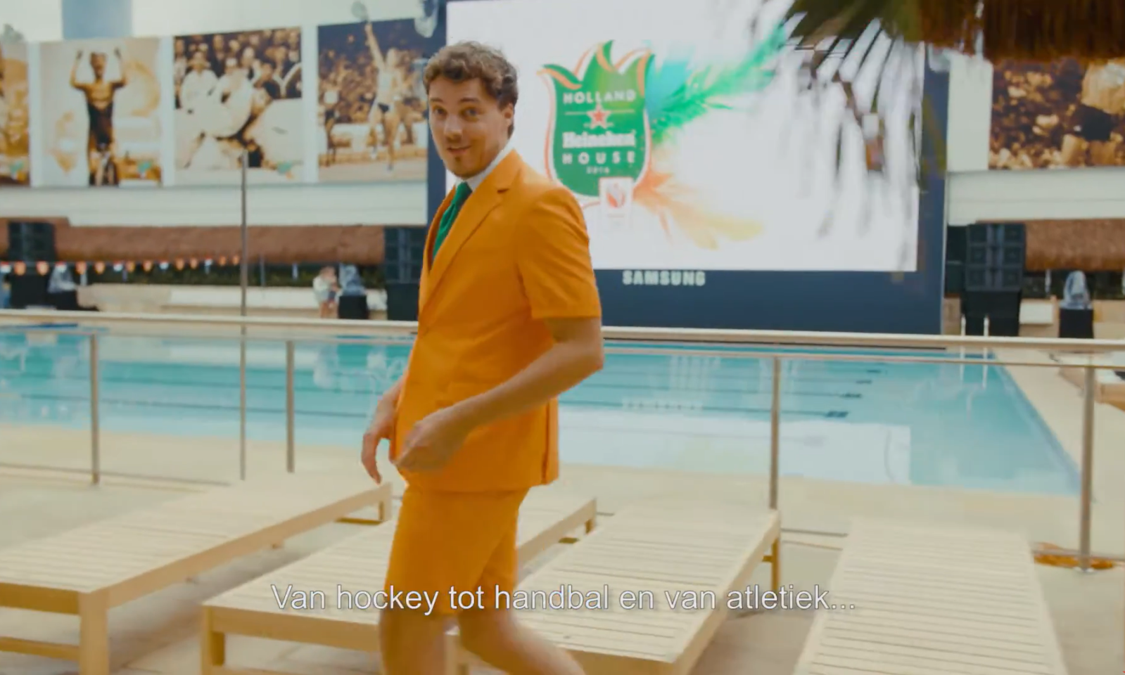 Man in oranje pak glimlacht bij zwembad in Holland Heineken House.
