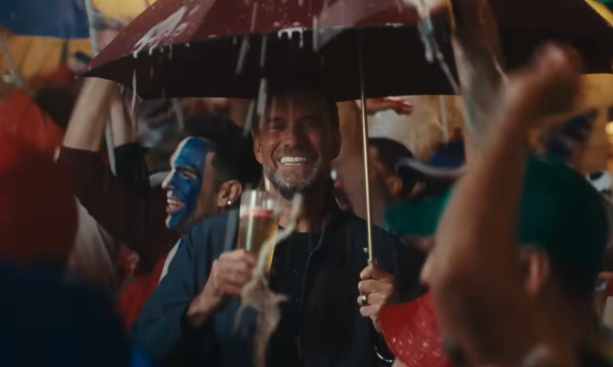 Klopp met paraplu en bier glimlacht te midden van juichende menigte.